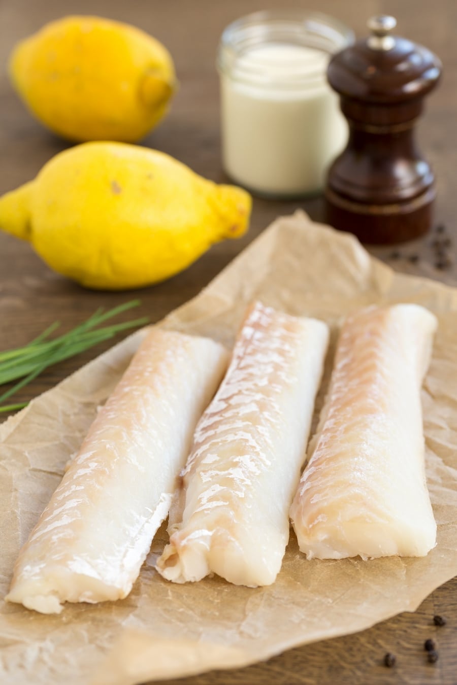 Cod fillets on a piece of parchment paper surrounded by other ingredients needed for the recipe.