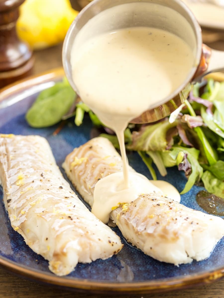 Pouring cream sauce over baked fish fillets.