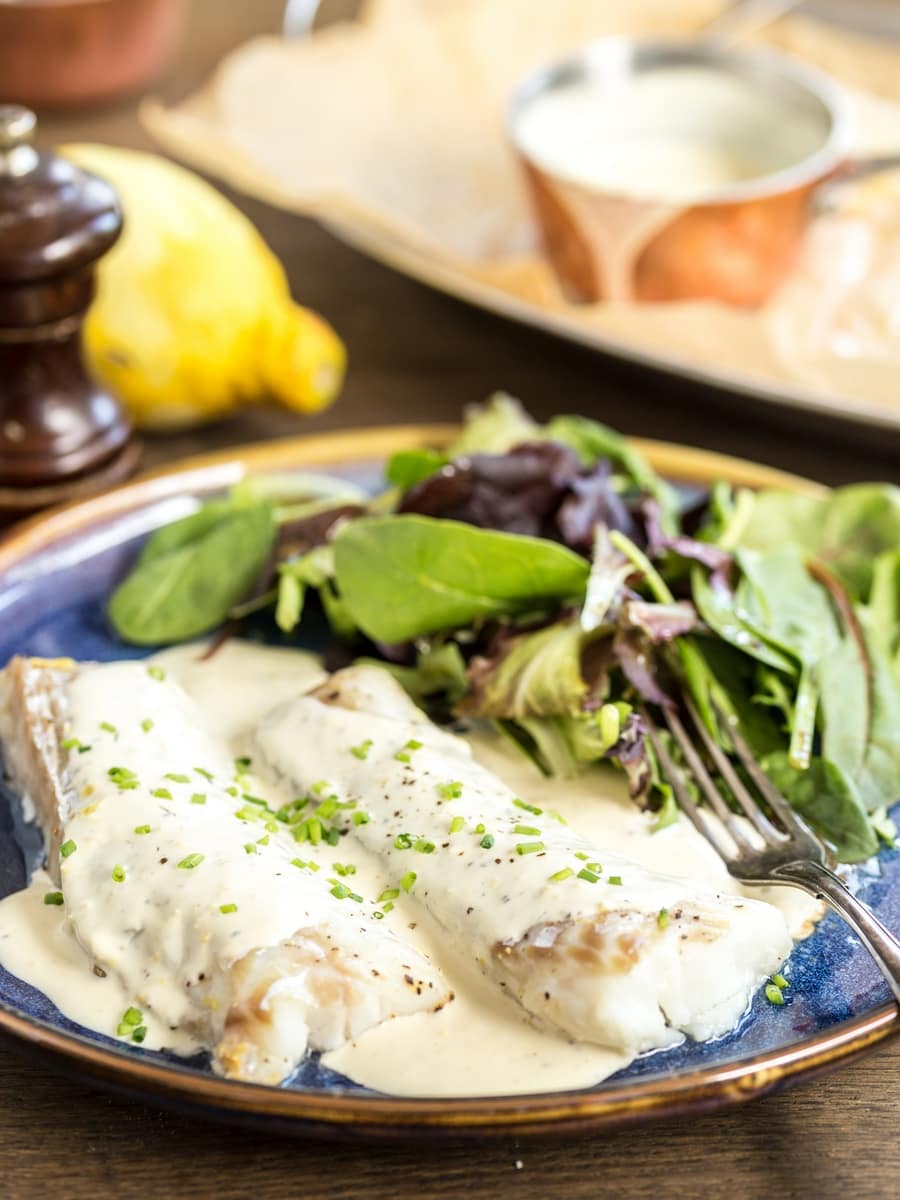 Baked lemon pepper cod with cream sauce served with a side of salad.