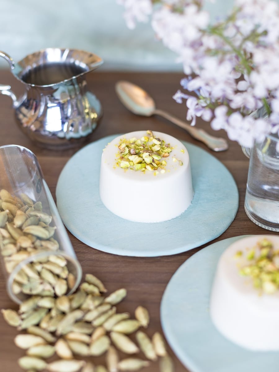 Vegan panna cotta with coconut milk and cardamom served on a blue plate with ground pistachio as decoration.