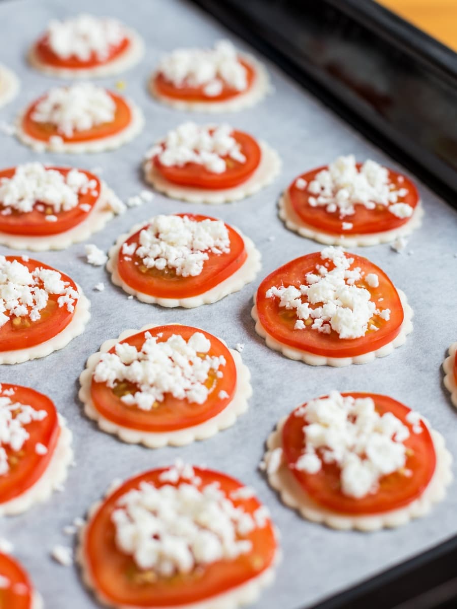 Placing fresh tomato and crumbled cheese on the puff pastry.