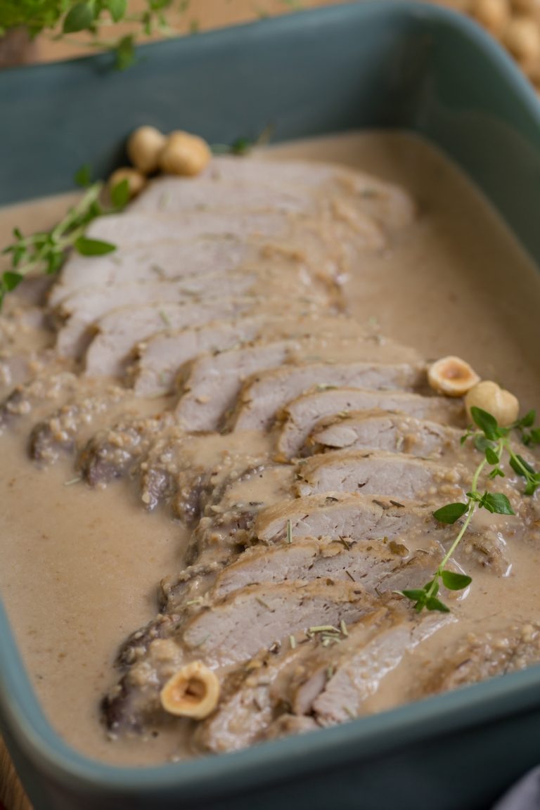 Baked pork loin in hazelnut sauce in green casserole dish.