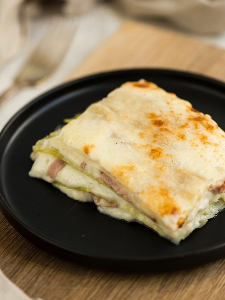 Slice of leek lasagna on black plate.