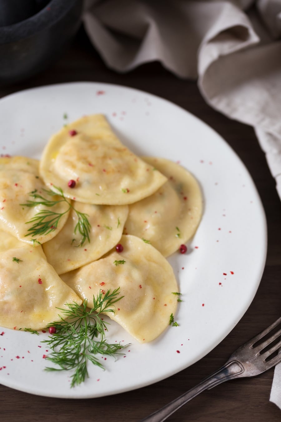 Smoked salmon ravioli with dill and pink peppercorns on a white plate.