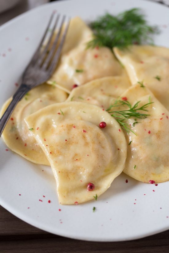 Smoked salmon ravioli with dill and pink peppercorns on a white plate.