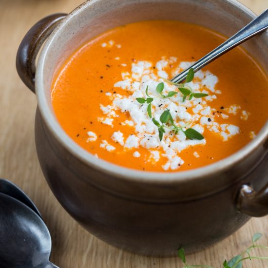 Orange pepper soup and white cheese crumbs in a brown clay pot, ladle in soup.