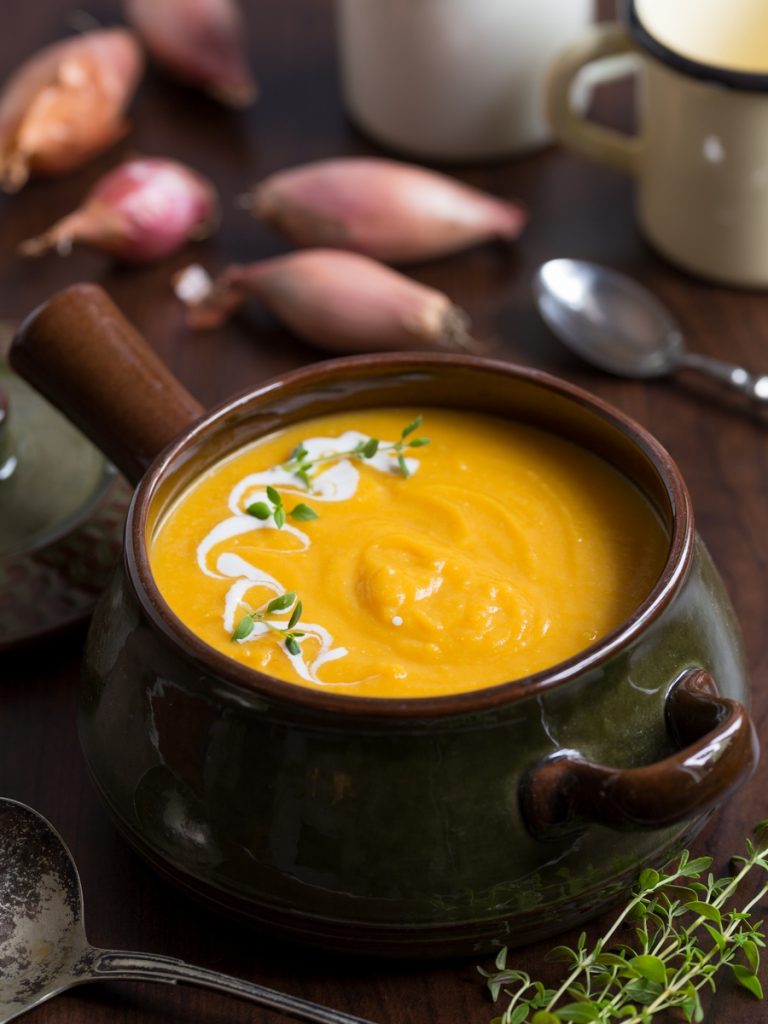 Pumpkin soup in a ceramic pot, shallots in the background.