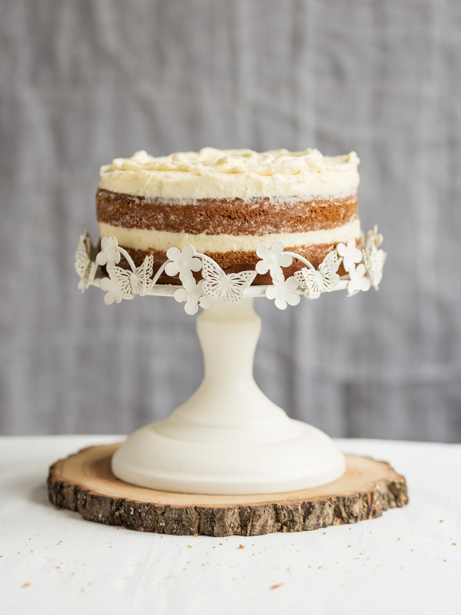 Sweet potato cake with brown butter frosting on white cake stand.