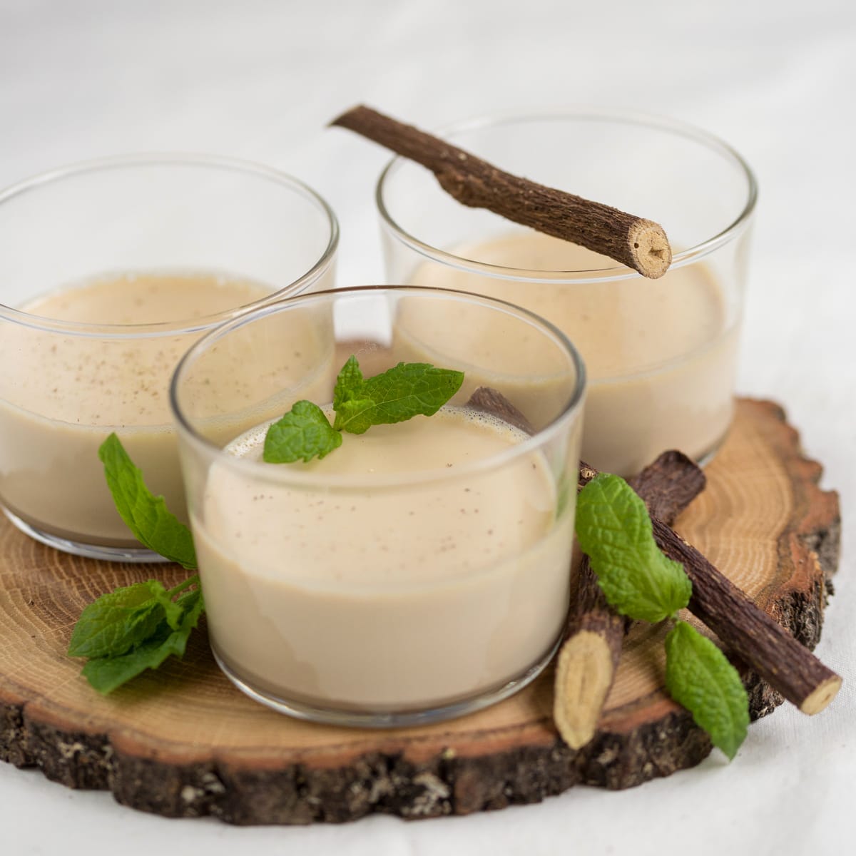 Liquorice panna cotta in three serving glasses on wooden tray.