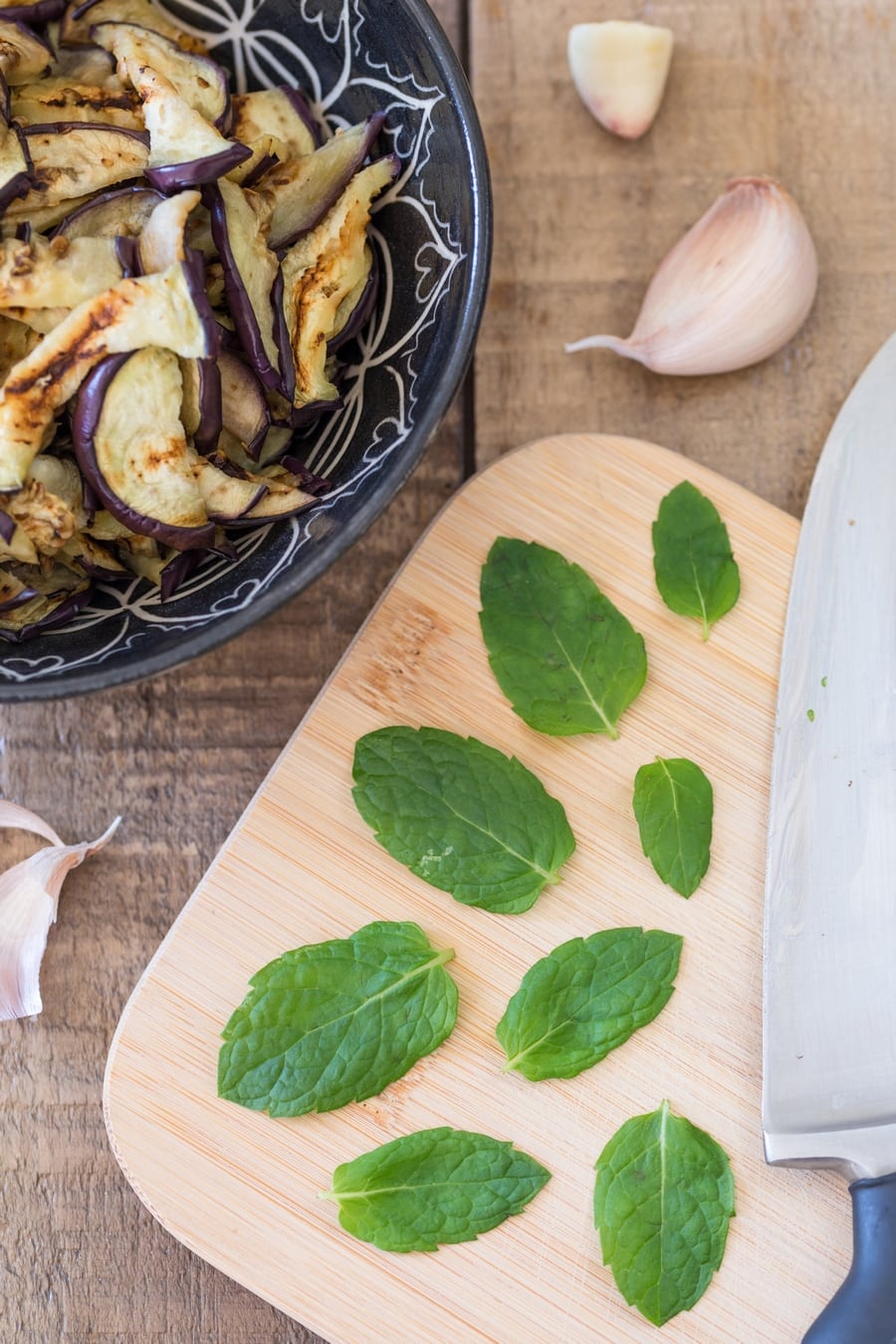Fresh spearmint leaves on a cutting board, sliced grilled eggplant on the side.
