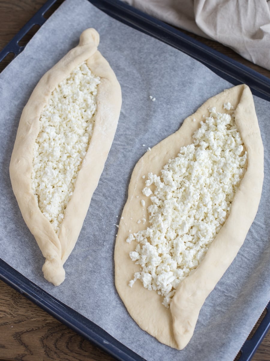 Raw sourdough khachapuri adjaruli in the making: folding the edges to create the boat shape.