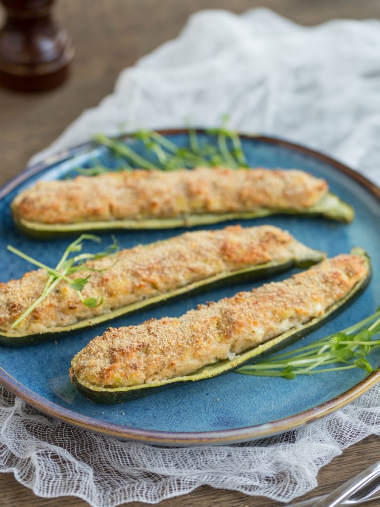 Baked zucchini boats with tuna and feta stuffing on blue plate.