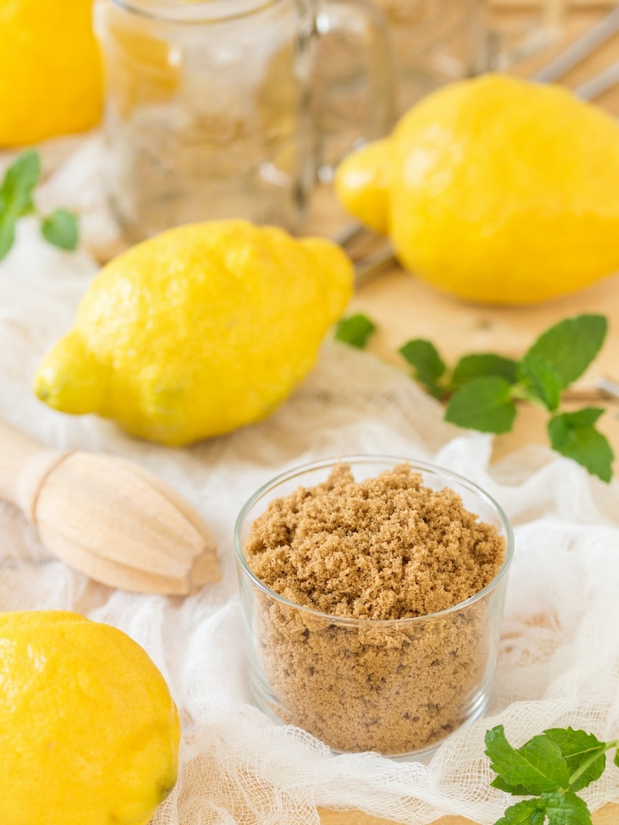 Muscovado sugar in a cup surrounded by lemons and mint leaves.
