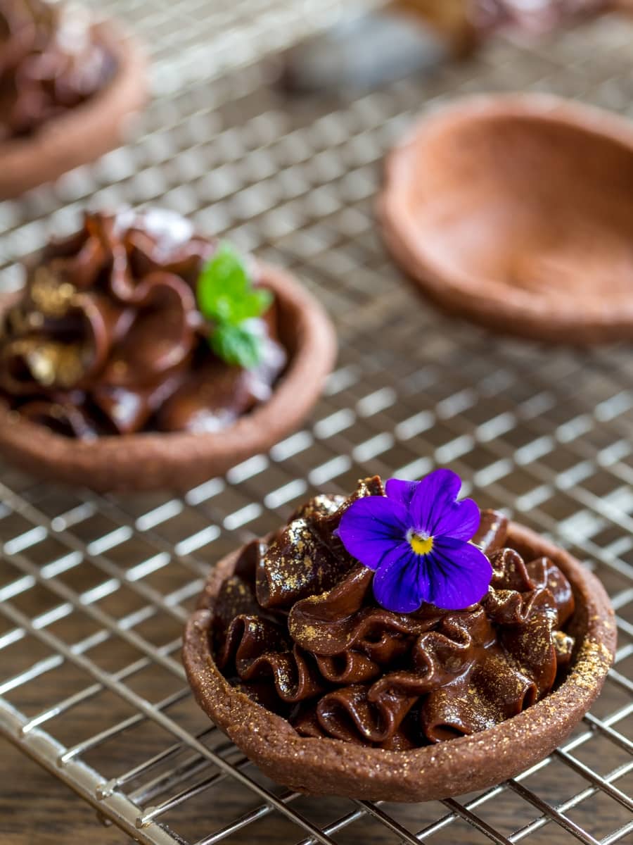 Chocolate mascarpone mousse tarts decorated with flowers and edible gold.