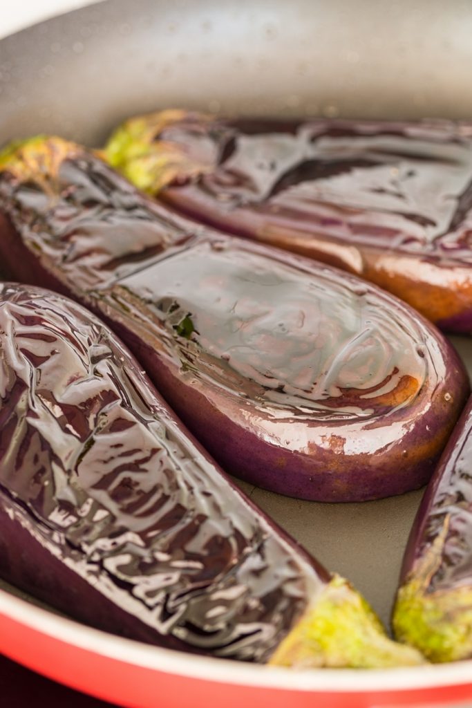 Eggplats cooking in a skillet, skin facing up.