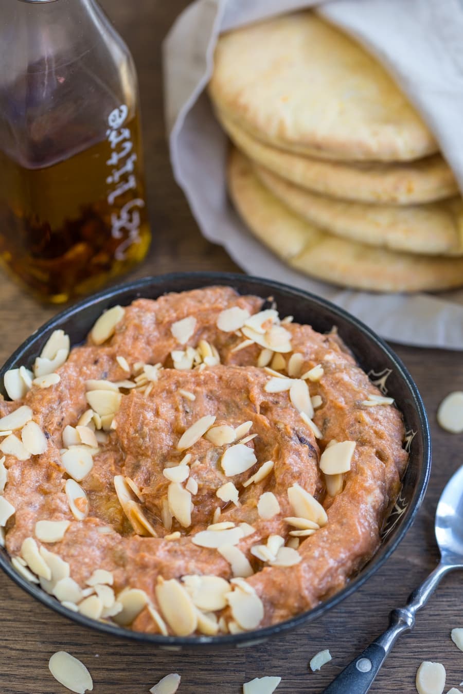 Eggplant ricotta dip garnished with roasted shaved almonds. Chili oil bottle and pita bread in the background.
