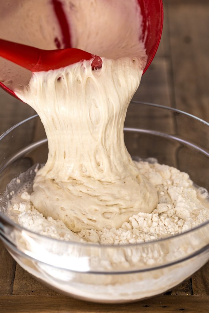 Adding poolish to flour and water mix to make pizza dough.