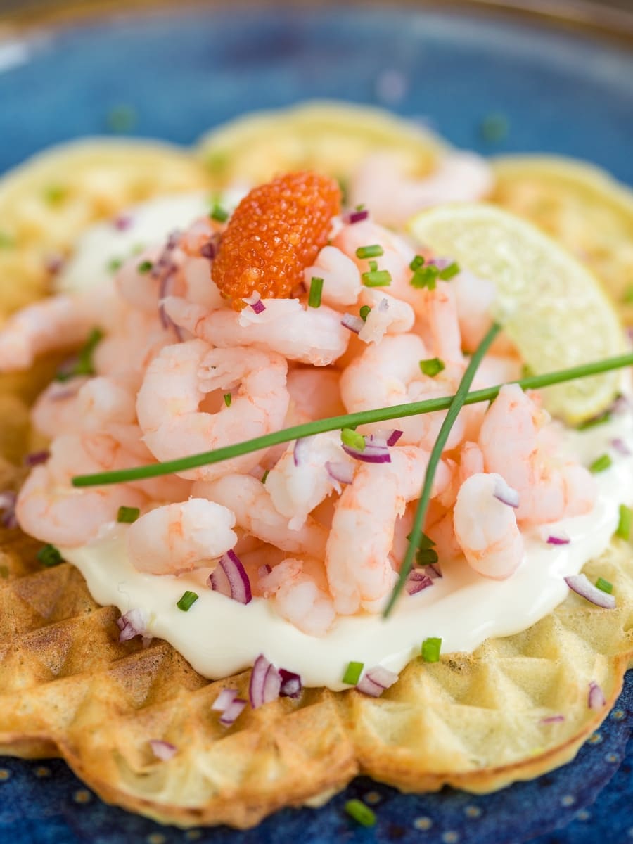 Sour cream waffle with shrimp topping decorated with chives and lemon slice.