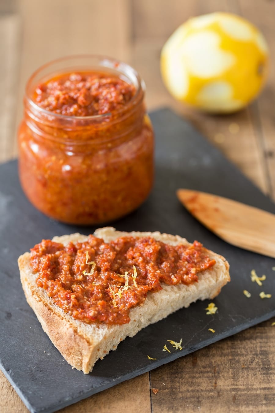 Piece of sourdough bread with sun-dried tomato pesto spread on top, pesto jar in the background.