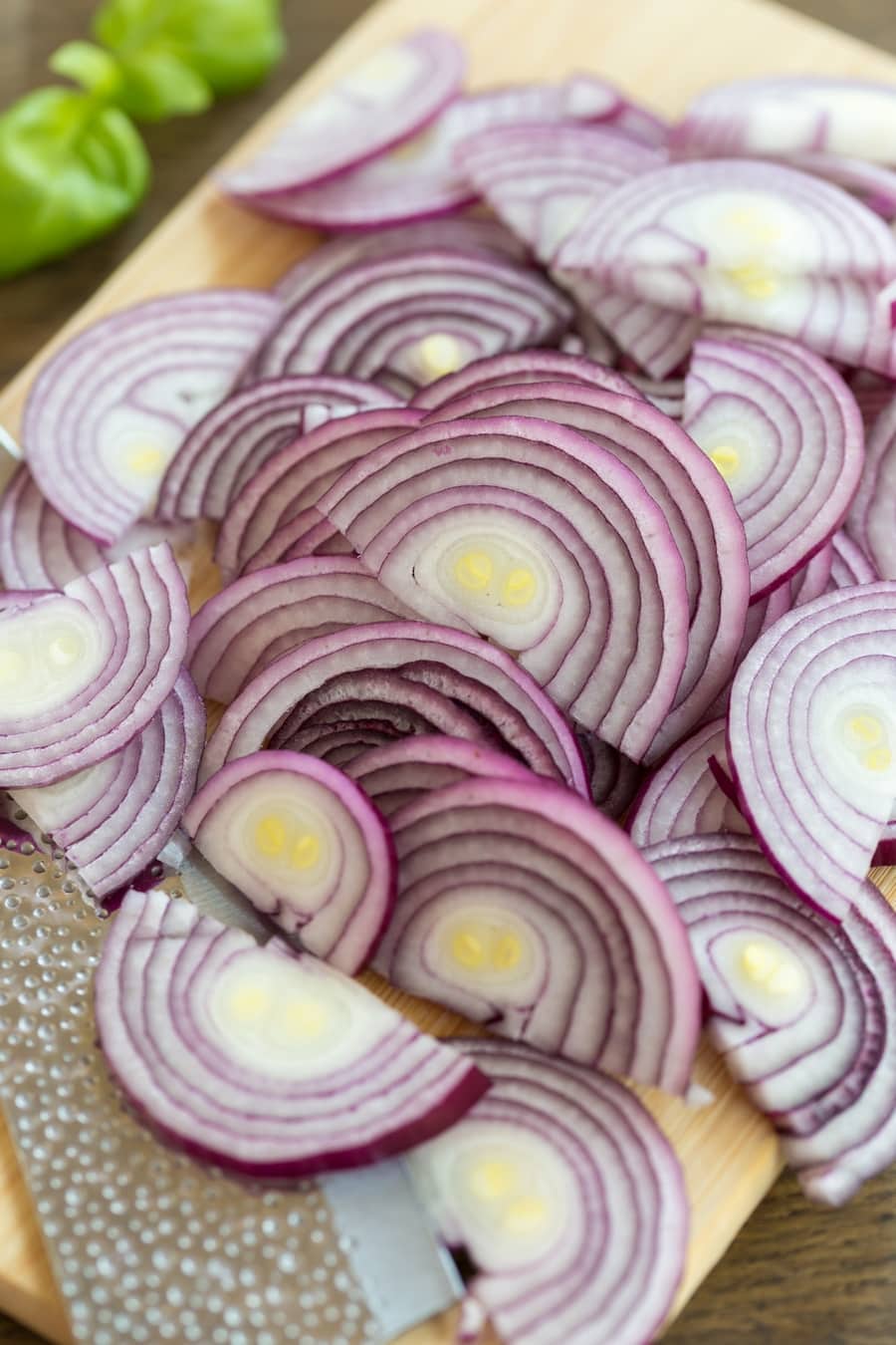 Sliced red onions on a wooden cutting board.