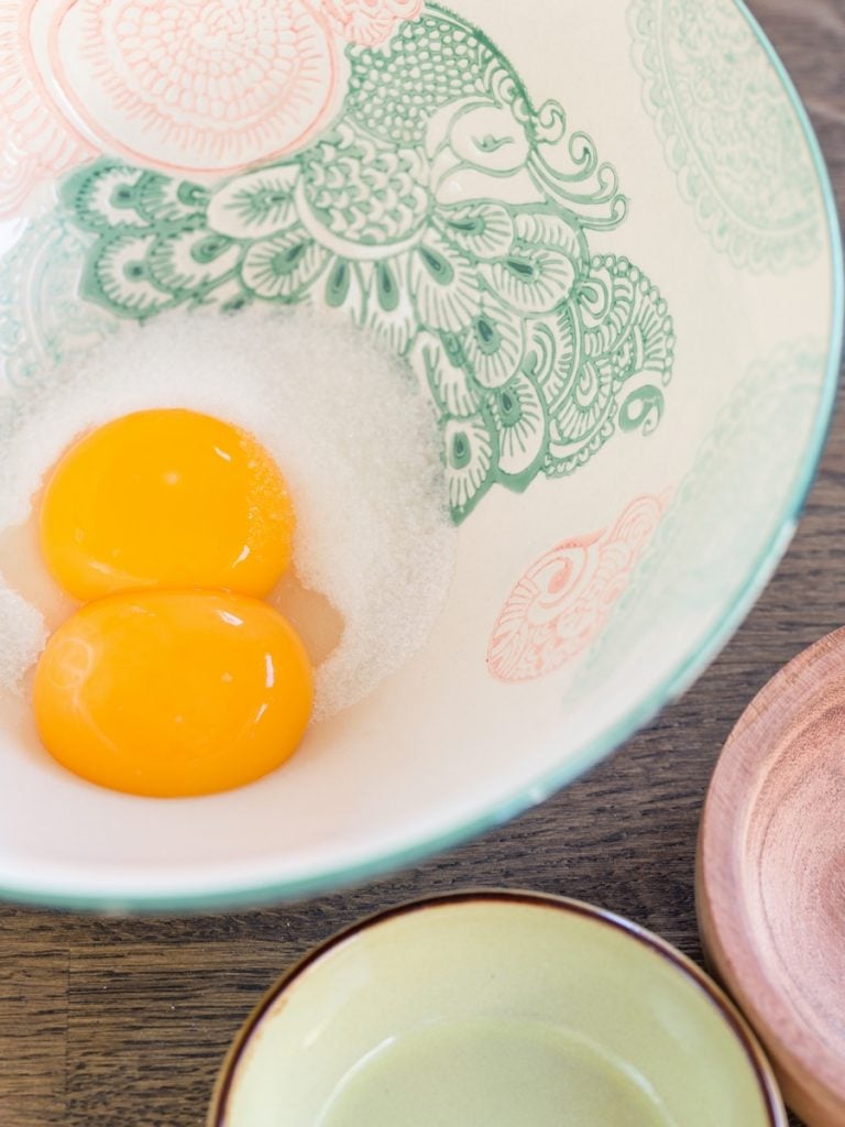 Two egg yolks in a bowl with granulated sugar.