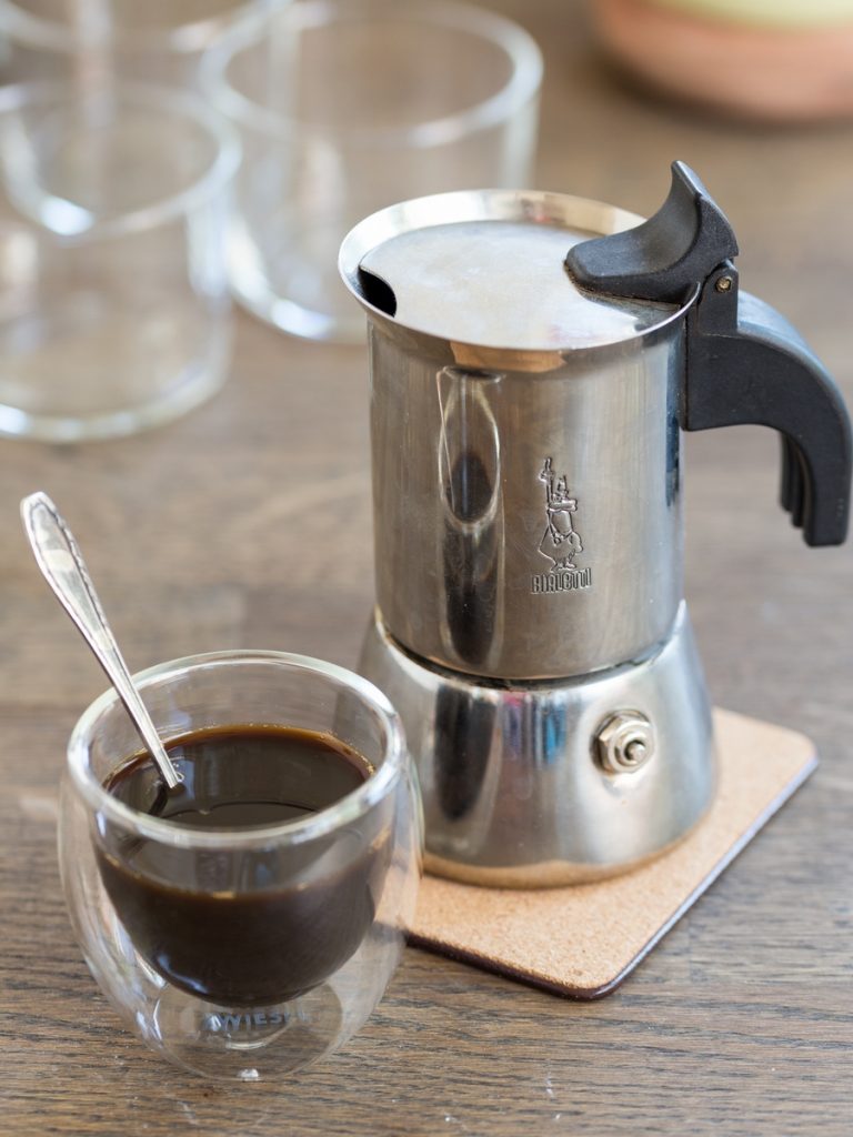 Bialetti moka pot and small see-through cup of coffee.