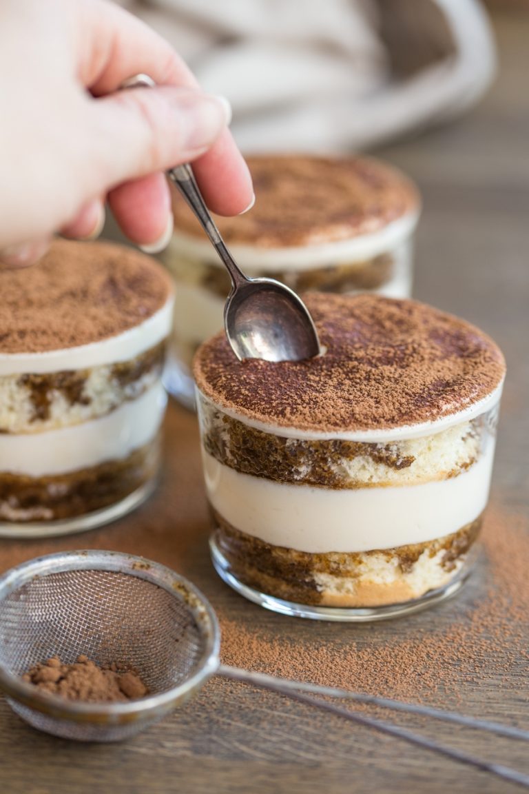 Spoon cutting through top layer of tiramisu in a glass.