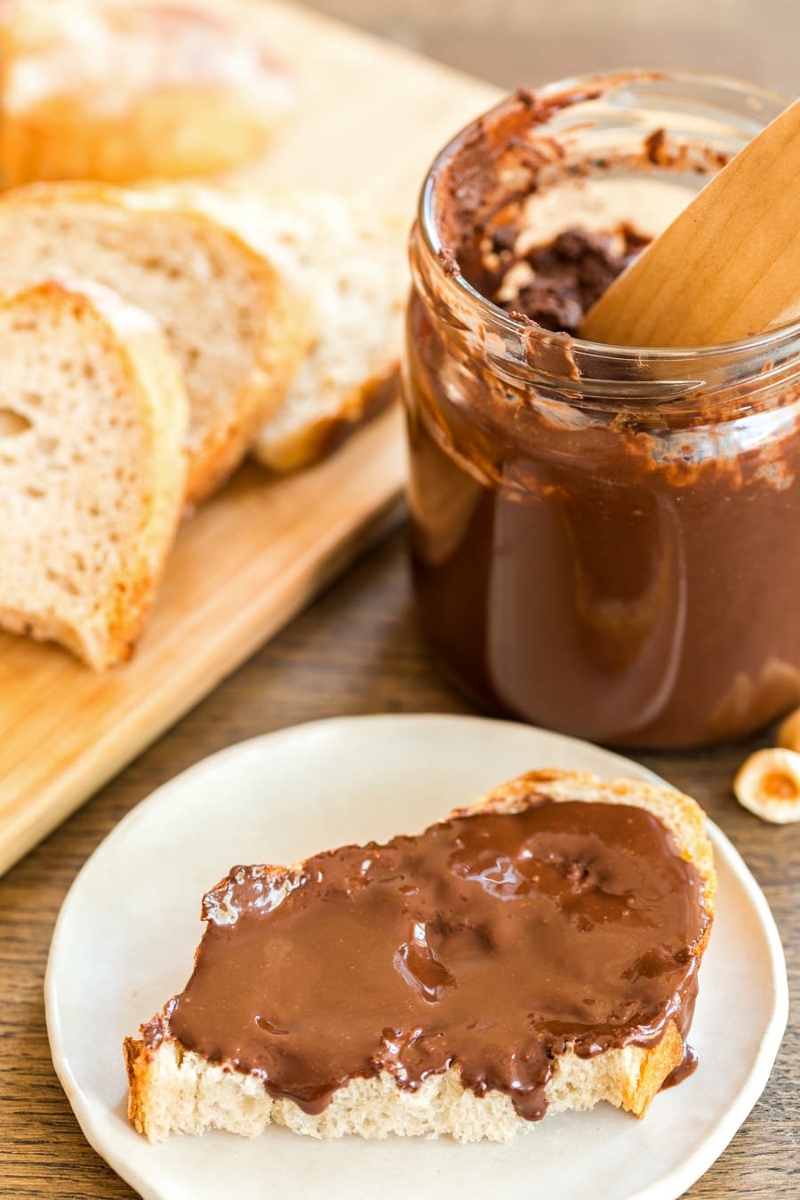 A jar of homemade dark chocolate nutella, some spread on the bread in front of it.