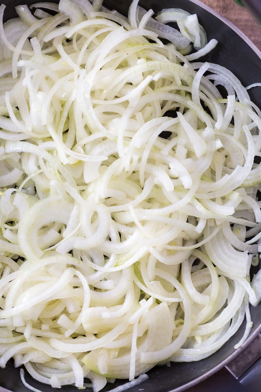 Raw yellow onions, sliced, in a skillet.
