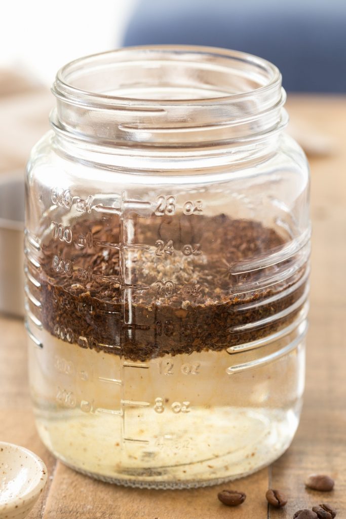 Ground coffee added to water in mason jar.