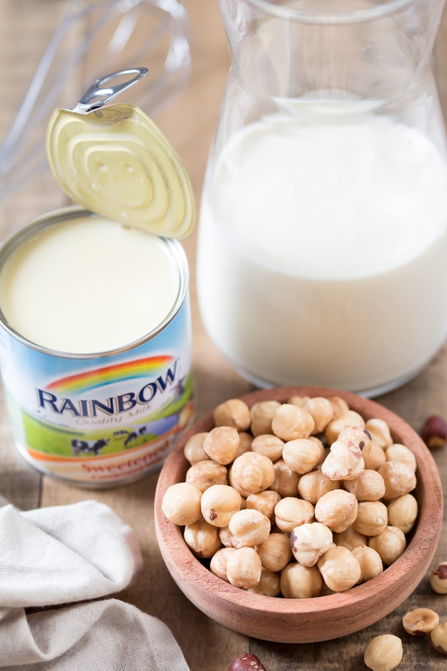Toasted hazelnuts in a bowl, can of condensed milk and cream in a vase.