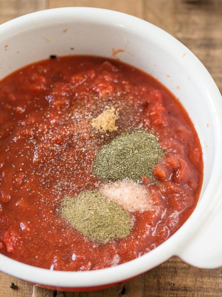Adding salt, sugar and dried herbs to a pot of tomato sauce.