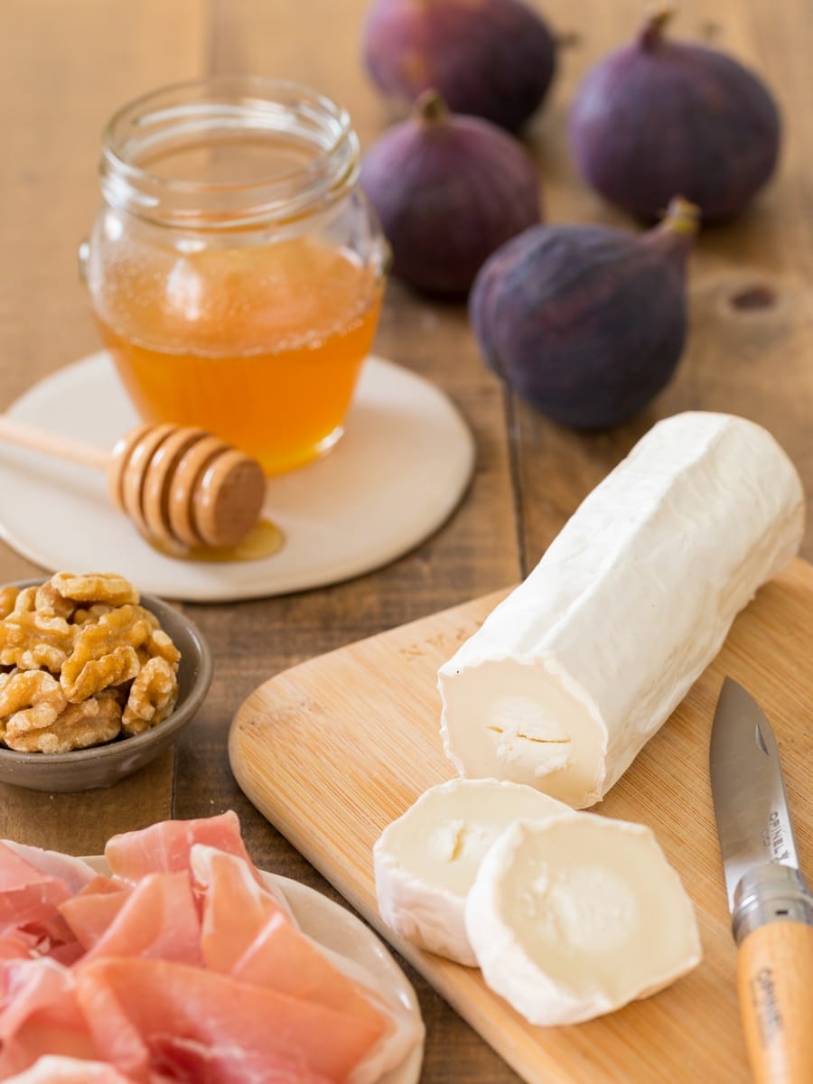 Goat log on a cutting board, prosciutto, walnuts, figs and honey in a jar.