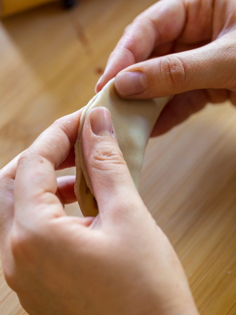 Hands sealing edge of pierogi.