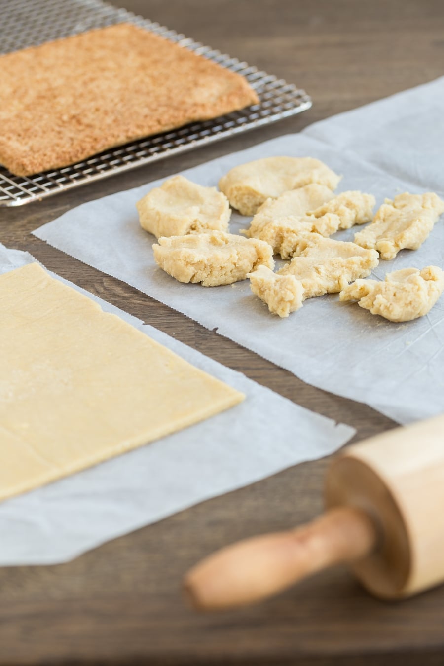 Crumbled pastry dough about to be rolled out between parchment paper sheets.