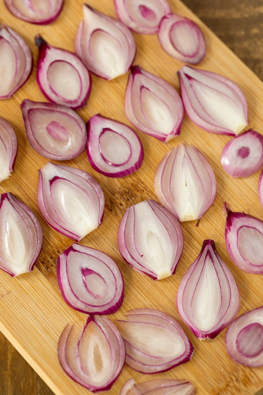 Thinly cut peral onions on a wooden cutting board.