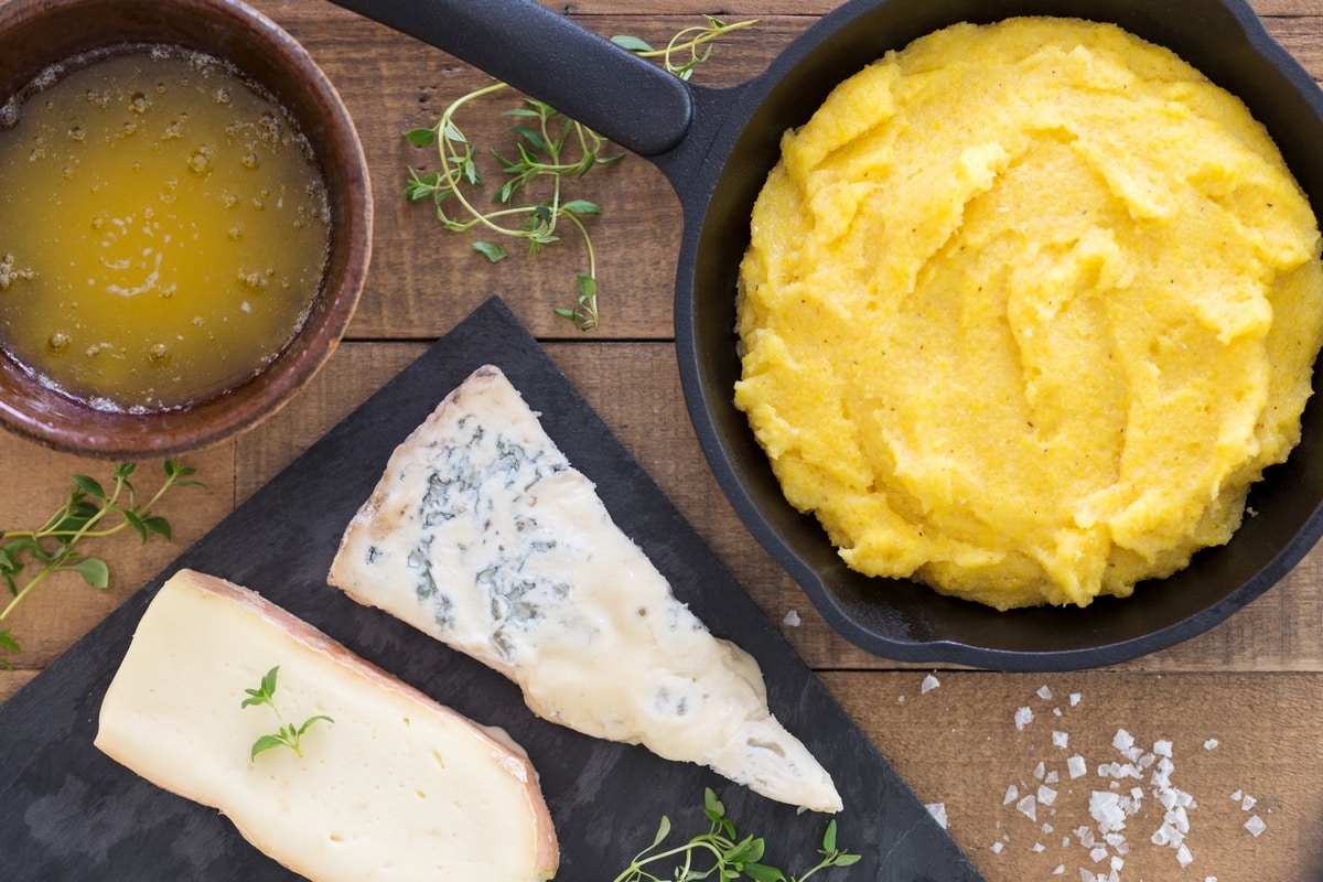 Polenta in a cast iron skillet, tray with taleggio and gorgonzola, bowl of melted butter.
