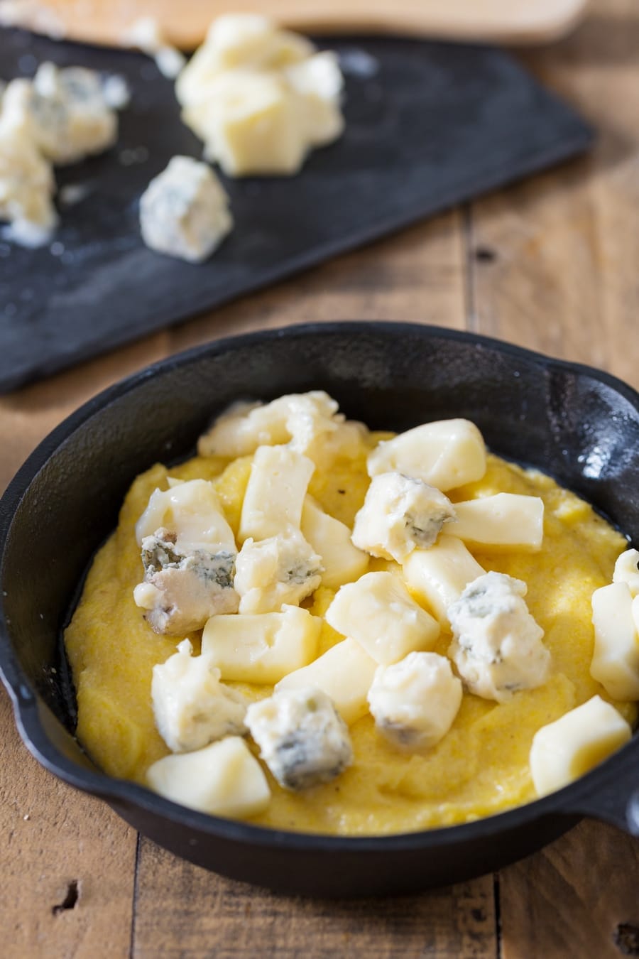 Polenta concia preparation: adding cubed cheese to polenta.