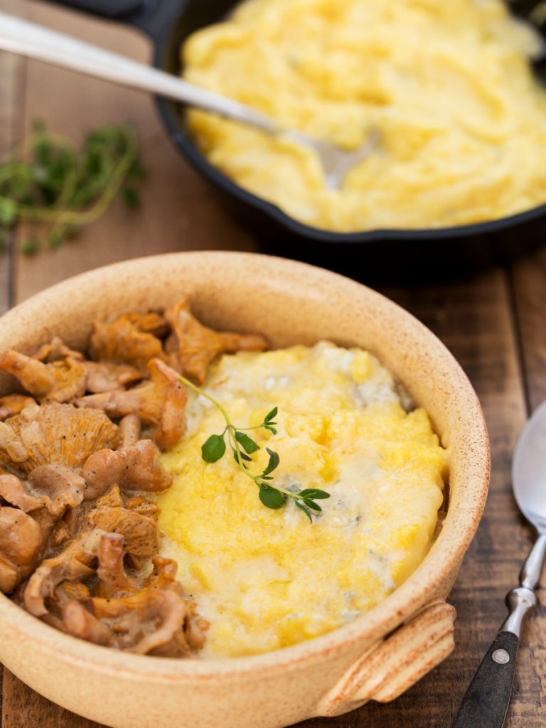 A portion of polenta concia with chanterelle sauce in a bowl.