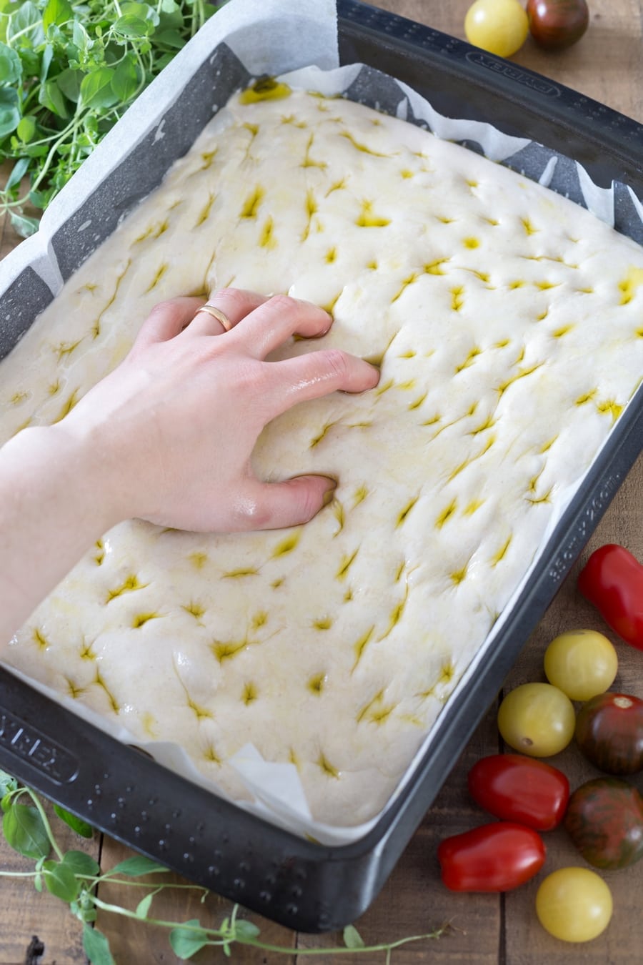 Oiled hand pressing holes into focaccia surface.