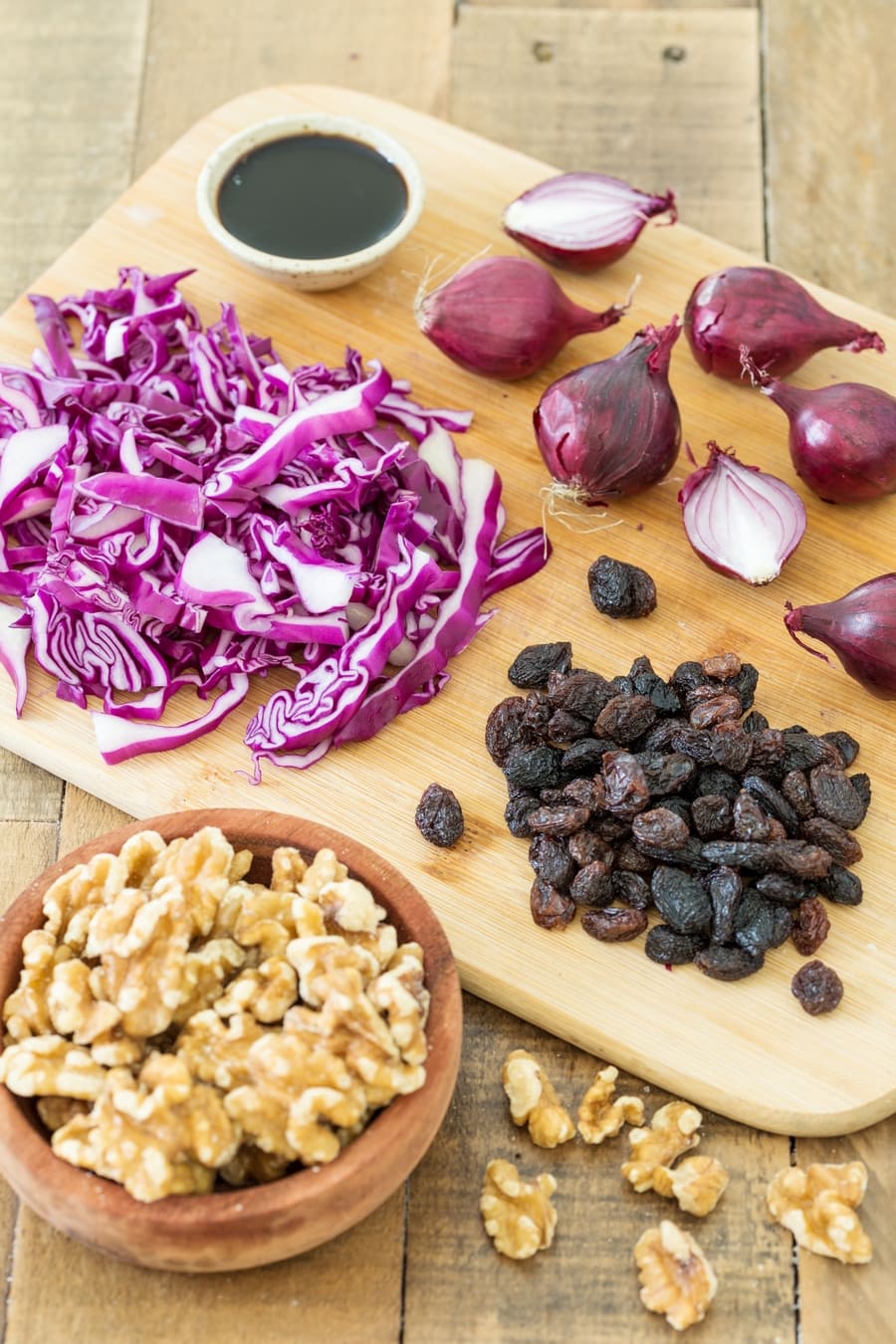 Shredded red cabbage, raisins, red onions on a chopping board, walnuts and balsamico in small bowls.