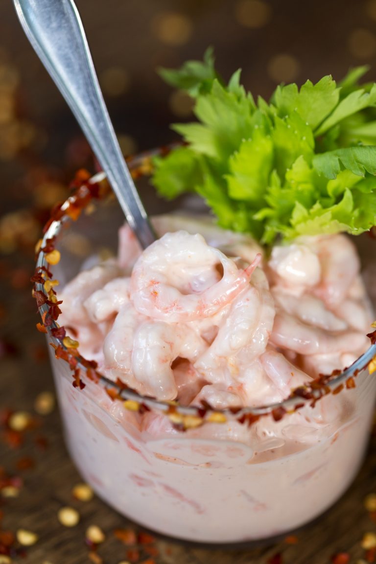 Chili flakes decorate the rim of a glass with shrimp in vodka sauce.