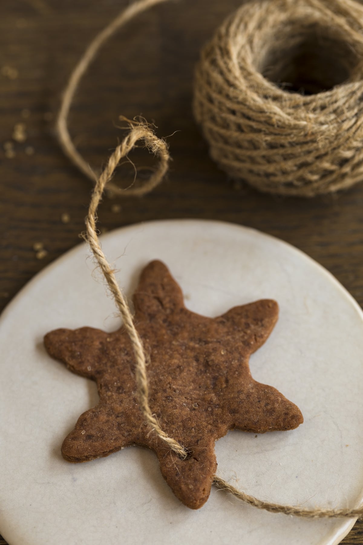 Jute twine being passed through a hole in a Swedish ginger thin cookie to use as Christmas tree ornament.