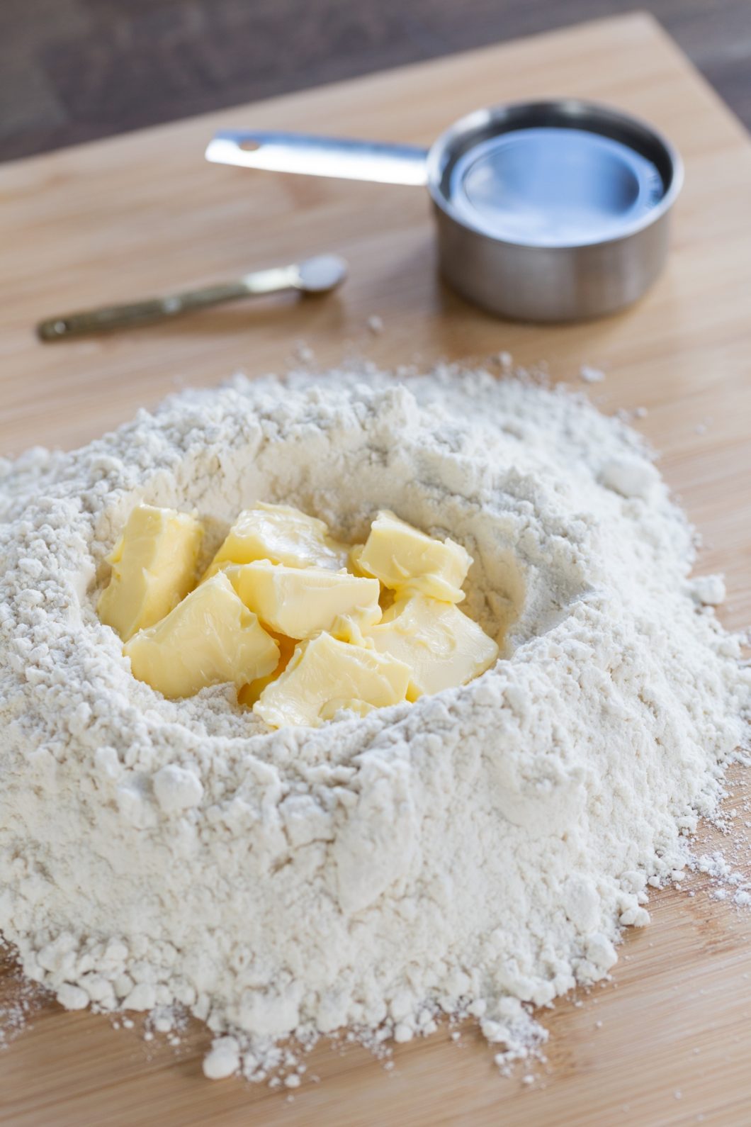 Mound of flour on a wooden surface, with cubed butter in the middle.