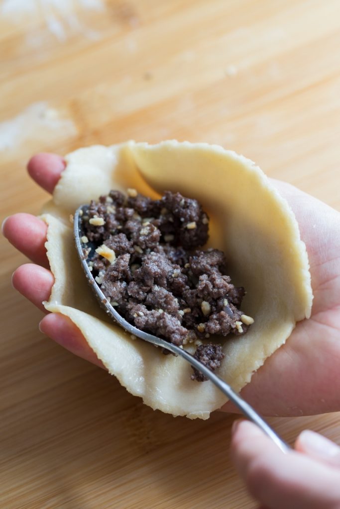 Filling pastry turnover in a hand with cooked meat.