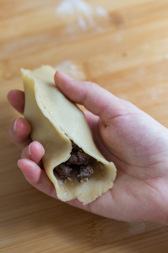 Hand pressing meat filling inside pastry dough to make turnover.