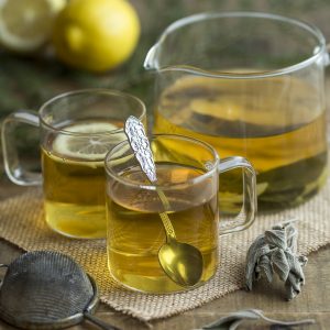 Lemon sage herbal tea in see-through jug and mugs.
