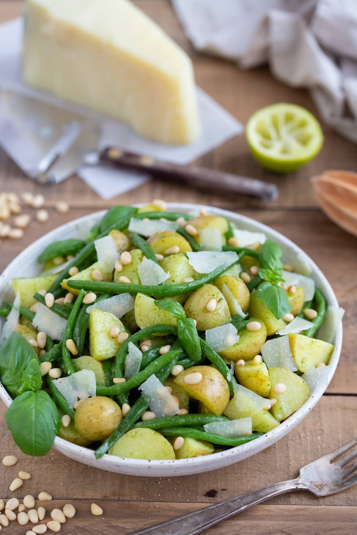 Pesto potato salad with green beans with a large chunk of pecorino in the background.