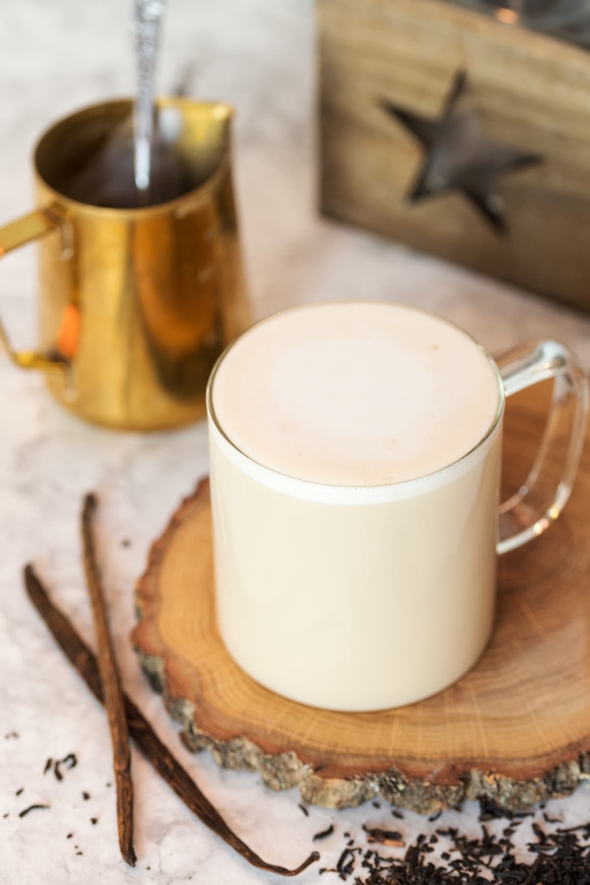 Earl Grey tea latte served in a see-through mug over a wooden tray.