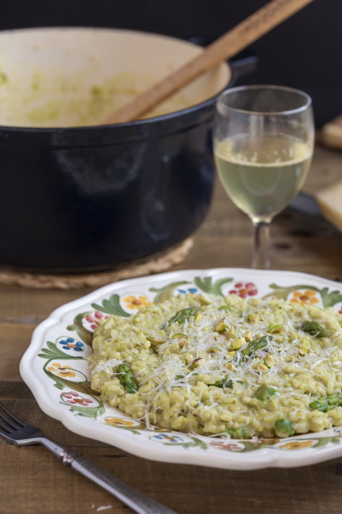A plate of asparagus risotto nest to a Dutch oven and a glass of white wine.